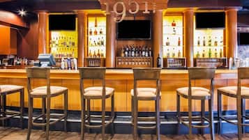 Zona de bar con un letrero que dice '1951', varias botellas de licor y taburetes.