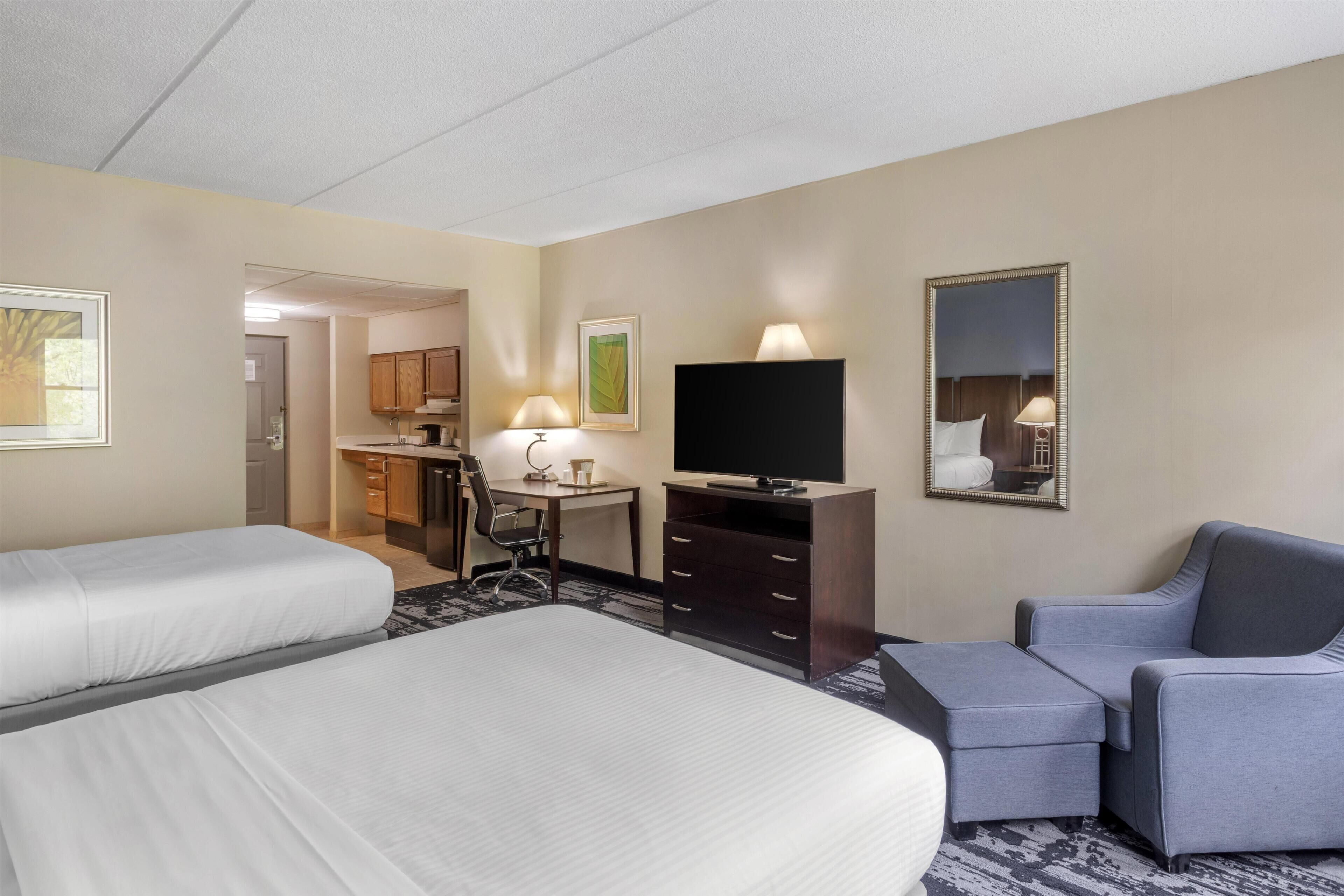 A hotel room with two beds, a desk, a chair, a TV, and a mirror.