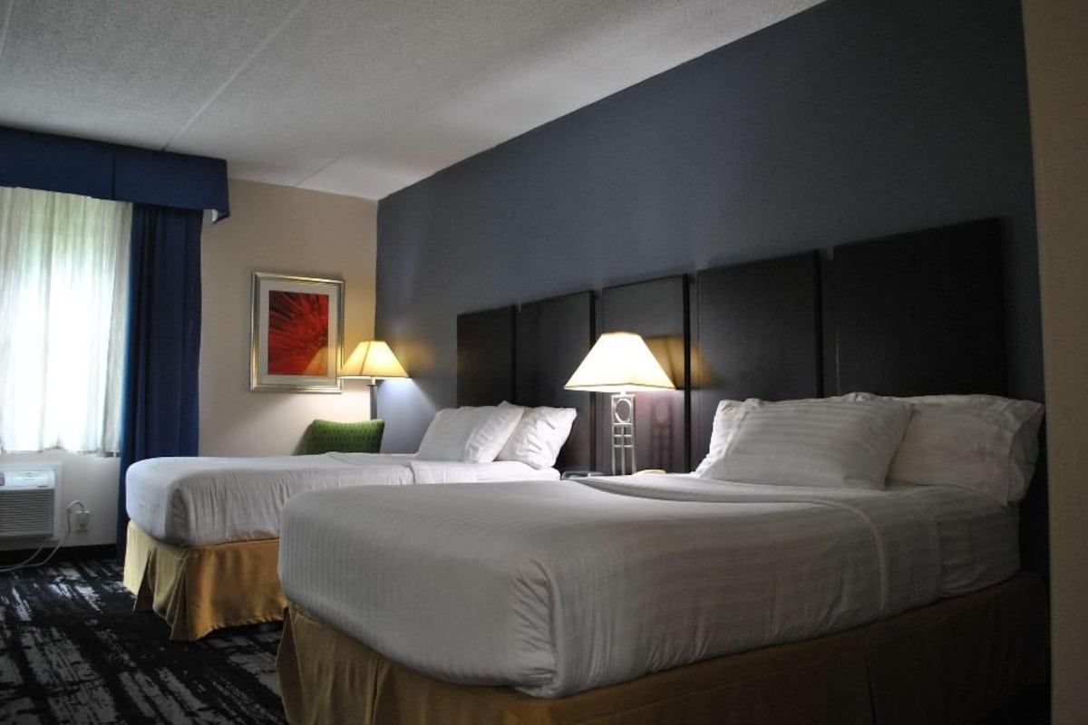 A hotel room with two beds, a window with curtains, a painting on the wall, and two bedside lamps.