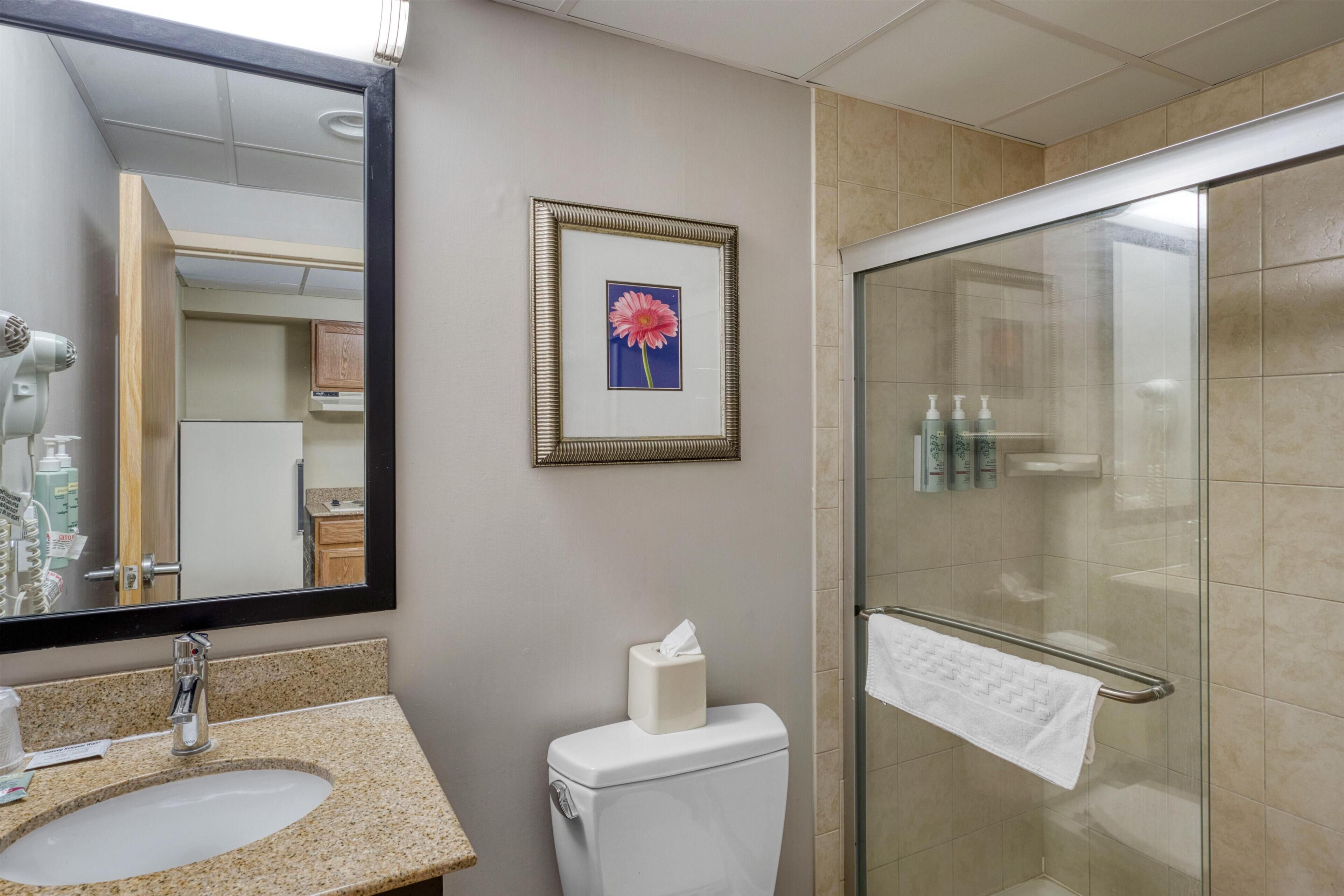 A bathroom with a sink, toilet, framed picture, and a glass shower enclosure.
