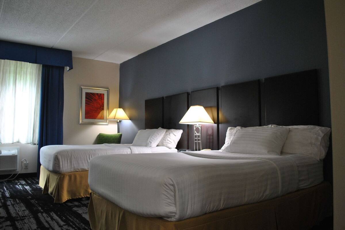 A hotel room with two beds, a window with curtains, a painting on the wall, and two bedside lamps.