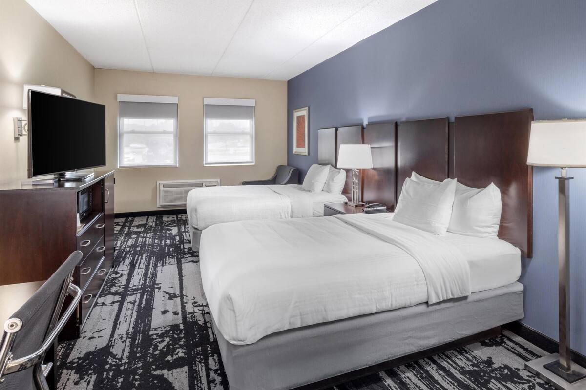 A hotel room with two beds, a flat-screen TV, a desk with a chair, and a lamp.