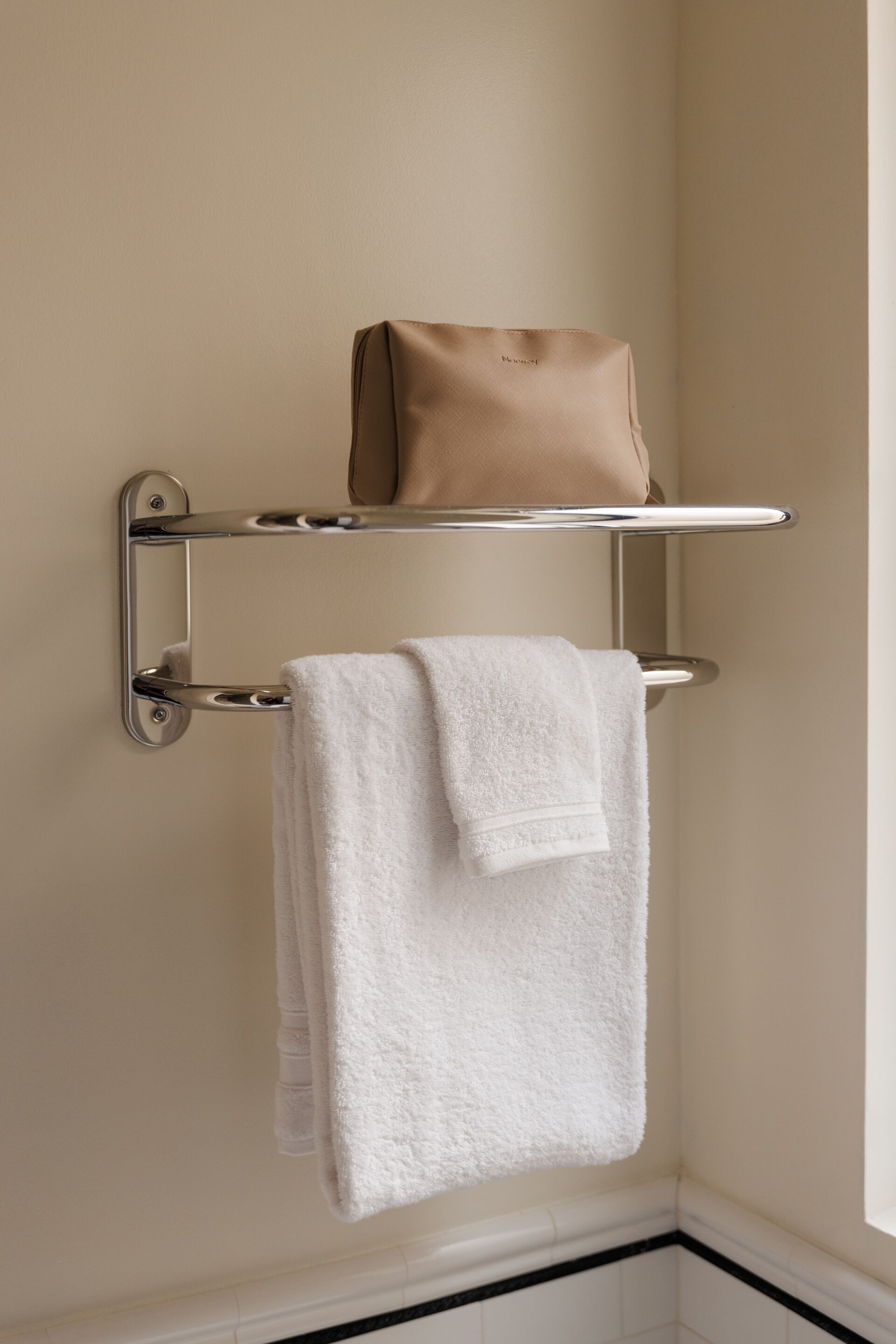 A bathroom with a towel rack holding a white towel and a beige bag on a shelf.