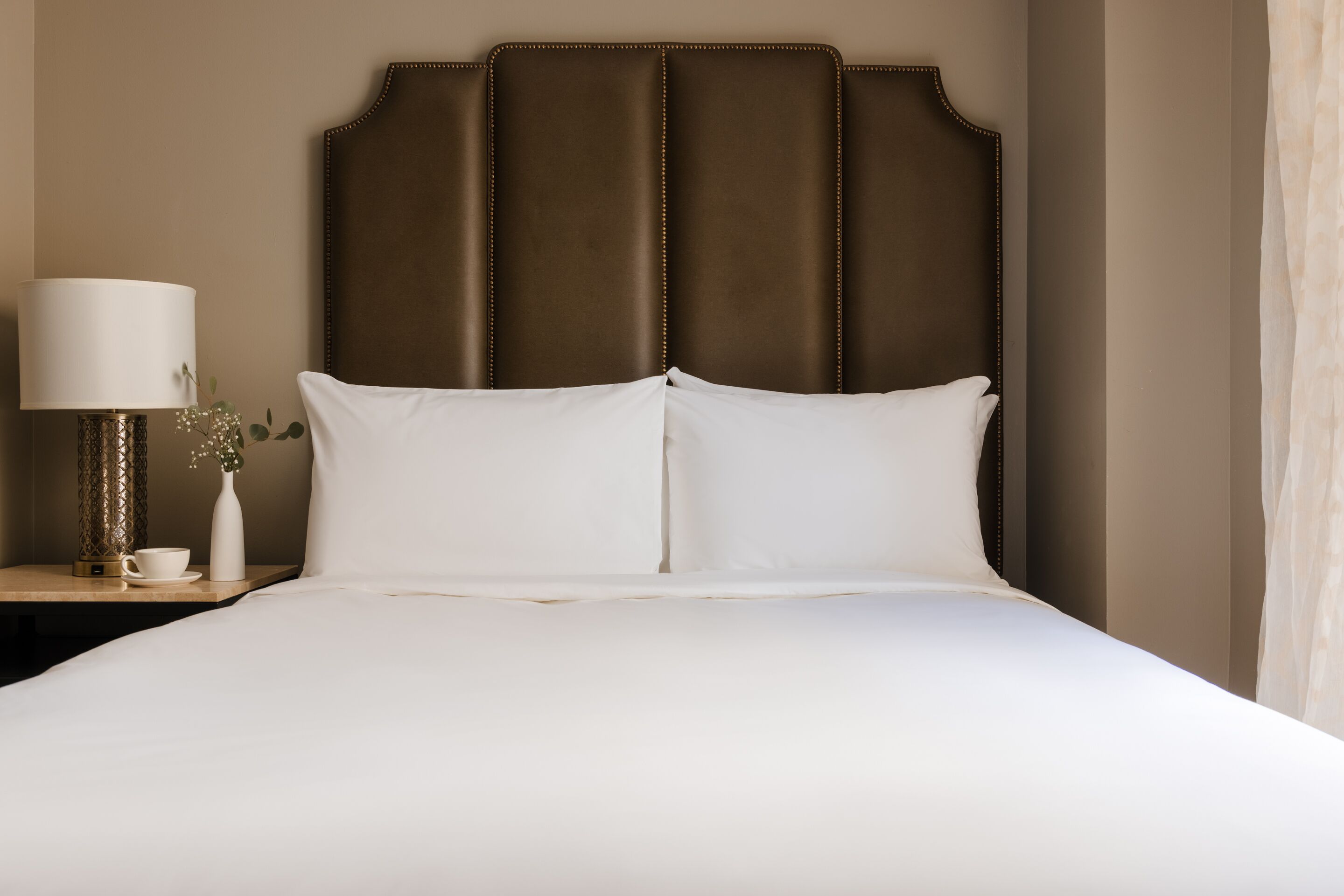 Una cama bien hecha con sábanas blancas y un cabecero tapizado en marrón.