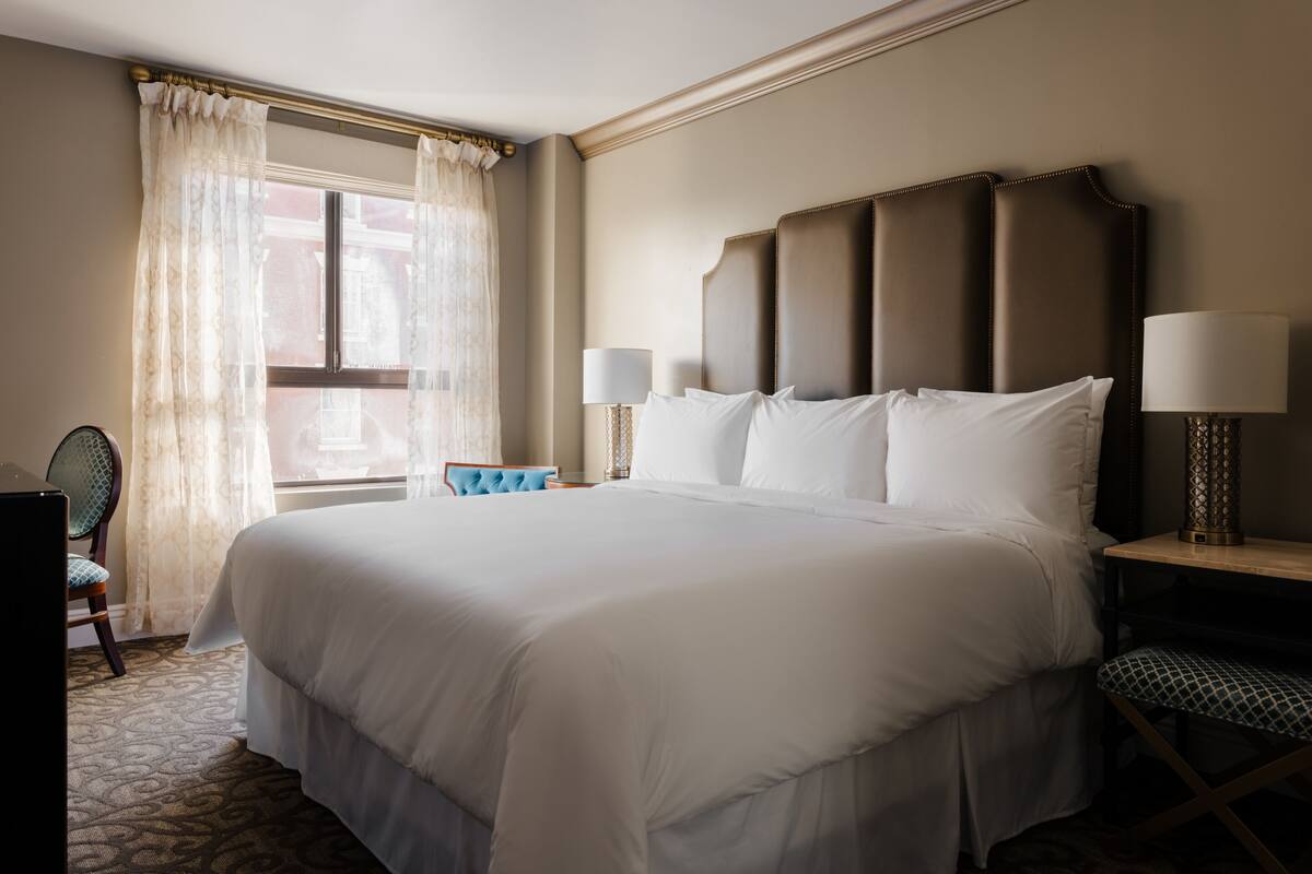 A hotel room with a large bed, two bedside lamps, a chair, and a window with curtains.