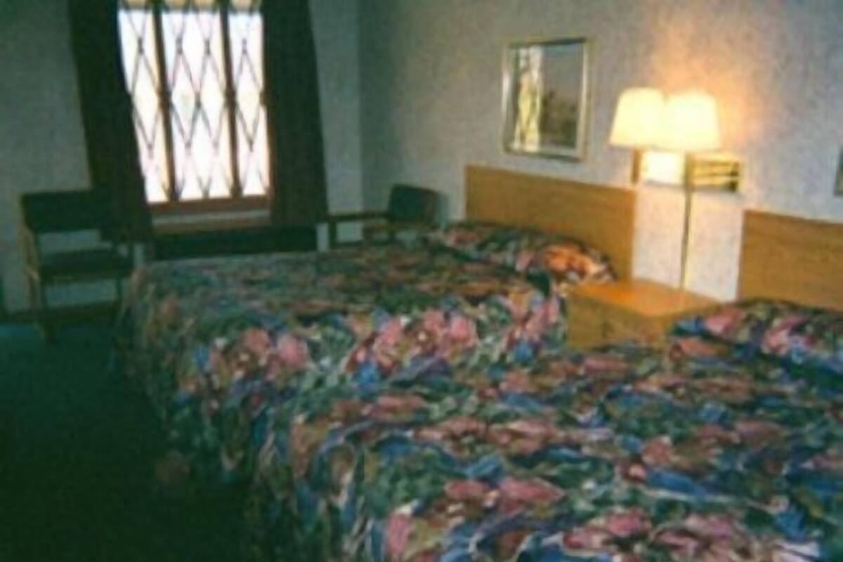 A hotel room with a bed, a chair, a lamp, and a window with a decorative grille.