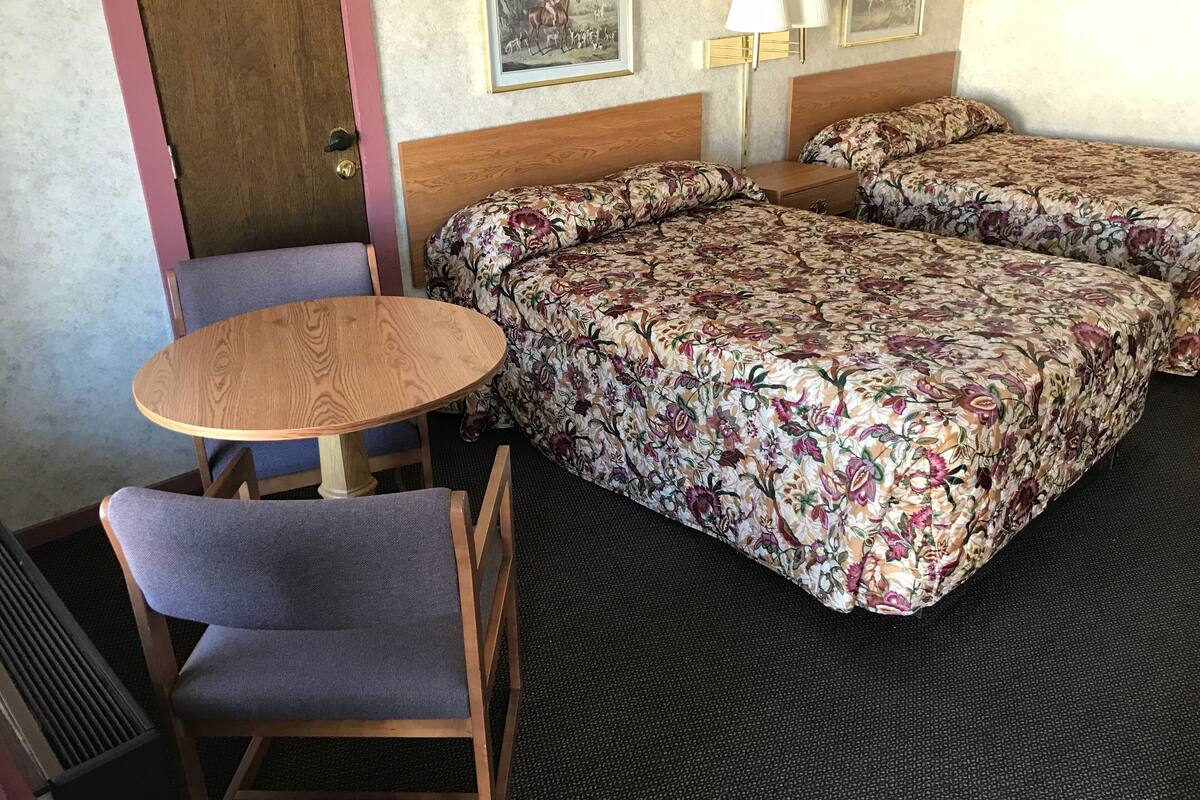 A hotel room with two beds, a wooden table, and a chair.