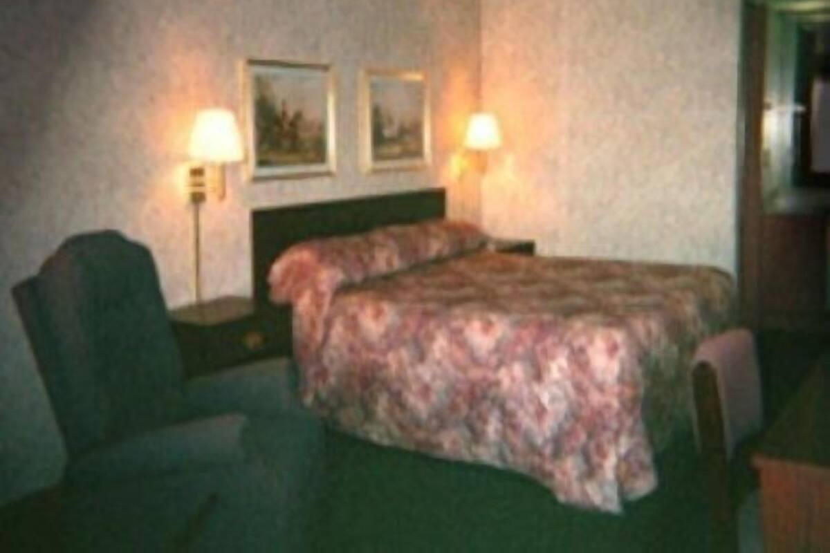 A hotel room with a bed, two bedside lamps, a chair, and a desk.