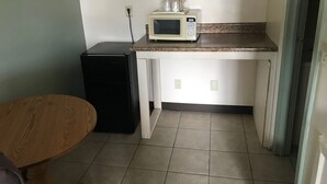 Una cocina compacta con microondas, un refrigerador pequeño y una mesa de madera.