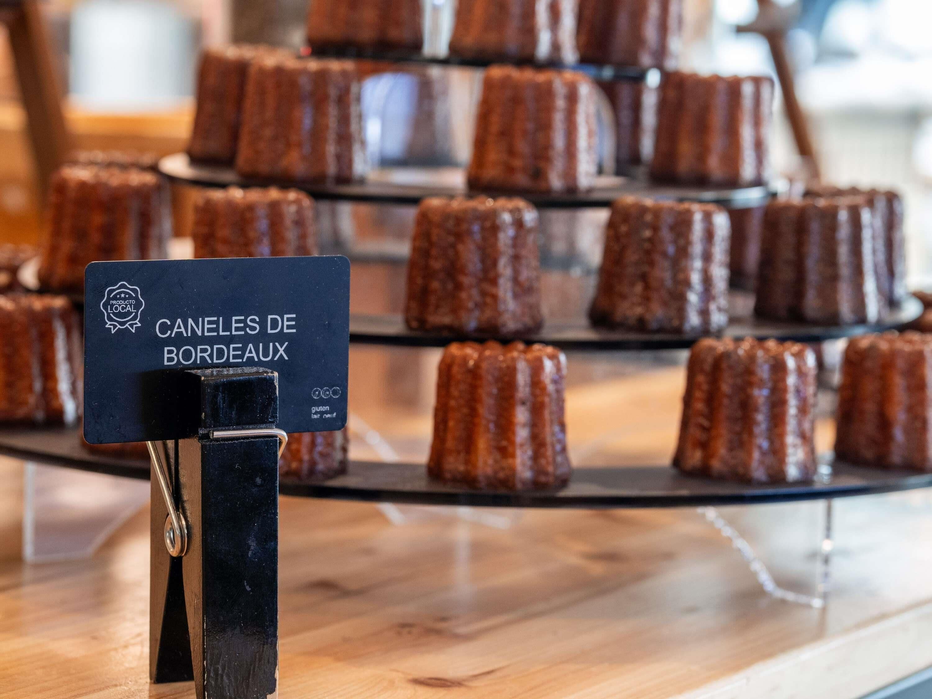 A display of canelés de bordeaux on a wooden table with a sign indicating they are gluten-free.