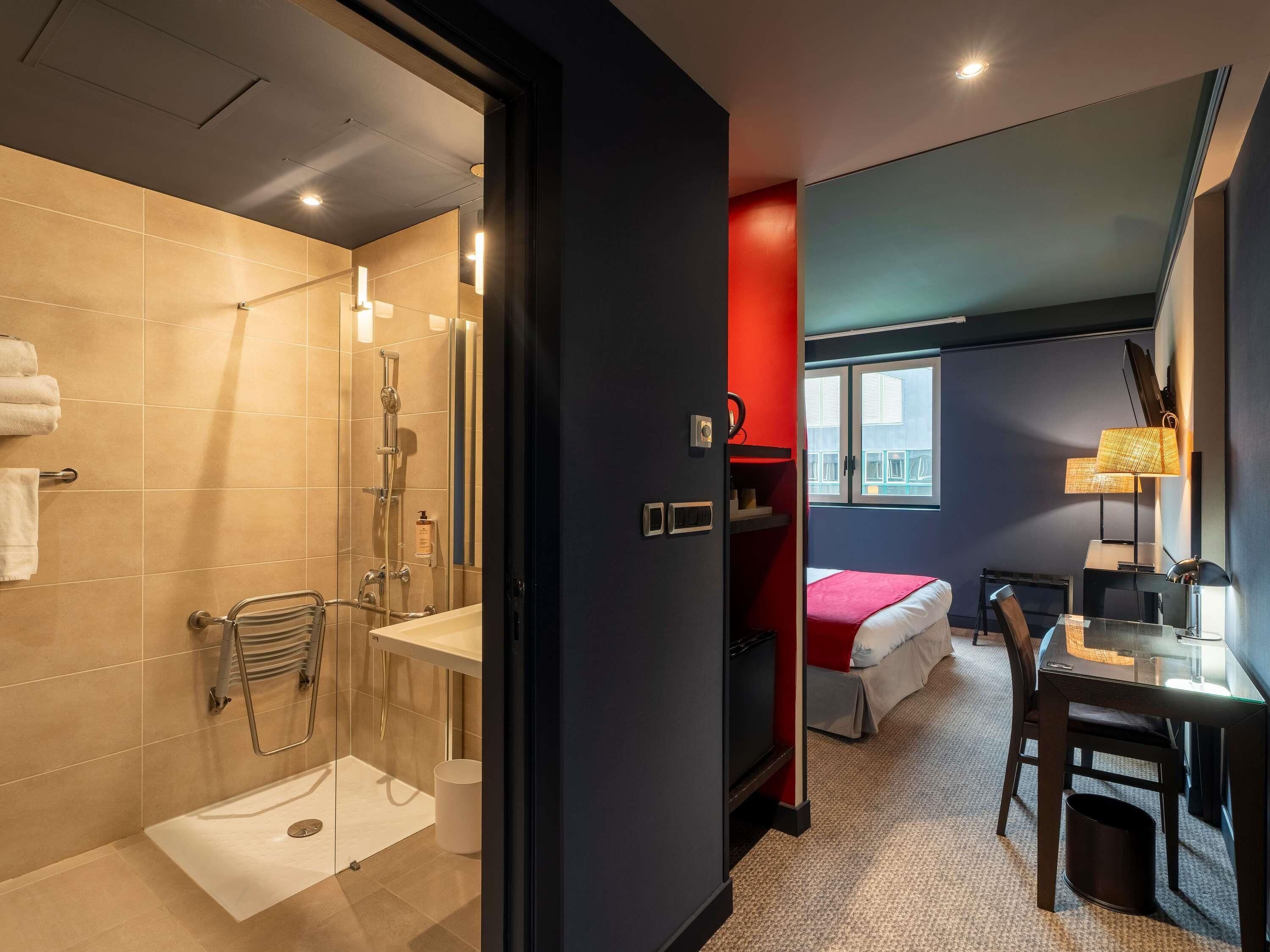 A modern hotel room with a shower, a bed, a desk, and a chair.