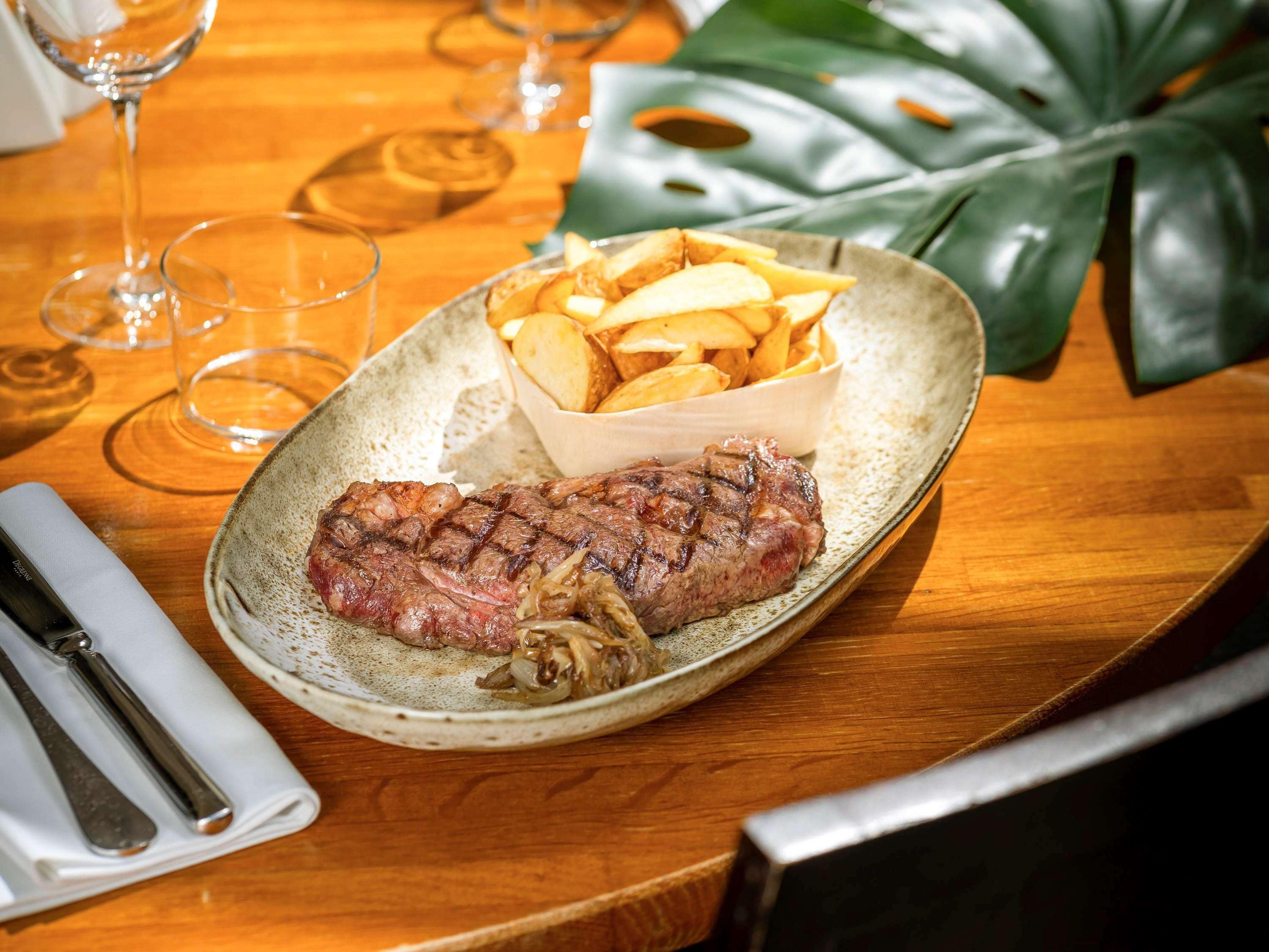 Un plato con un bistec y papas fritas sobre una mesa de madera.