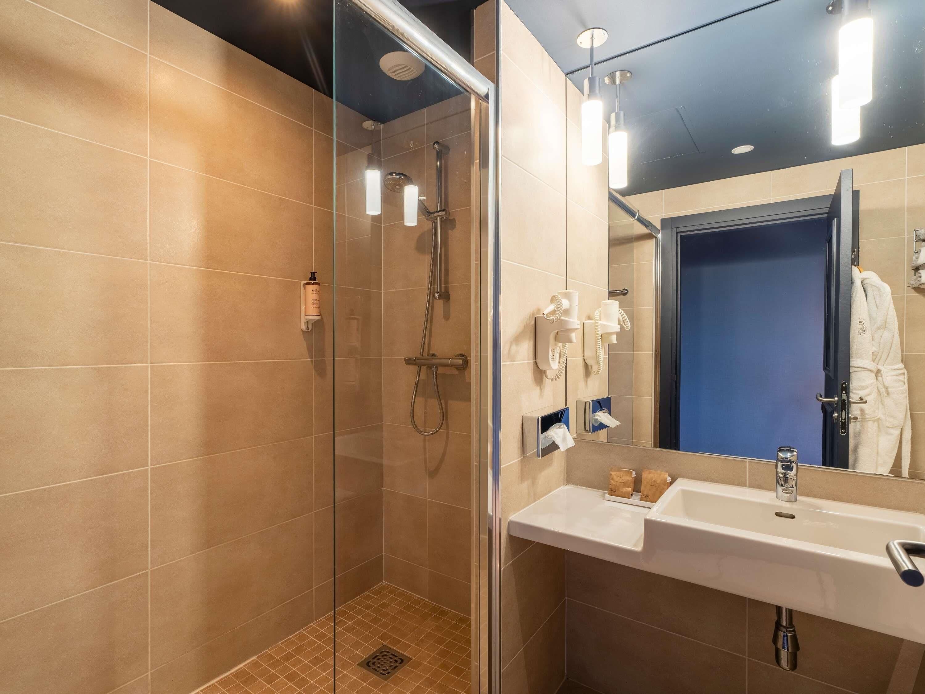 A modern bathroom with a glass-enclosed shower, a white sink, and a mirror with a blue door in the background.