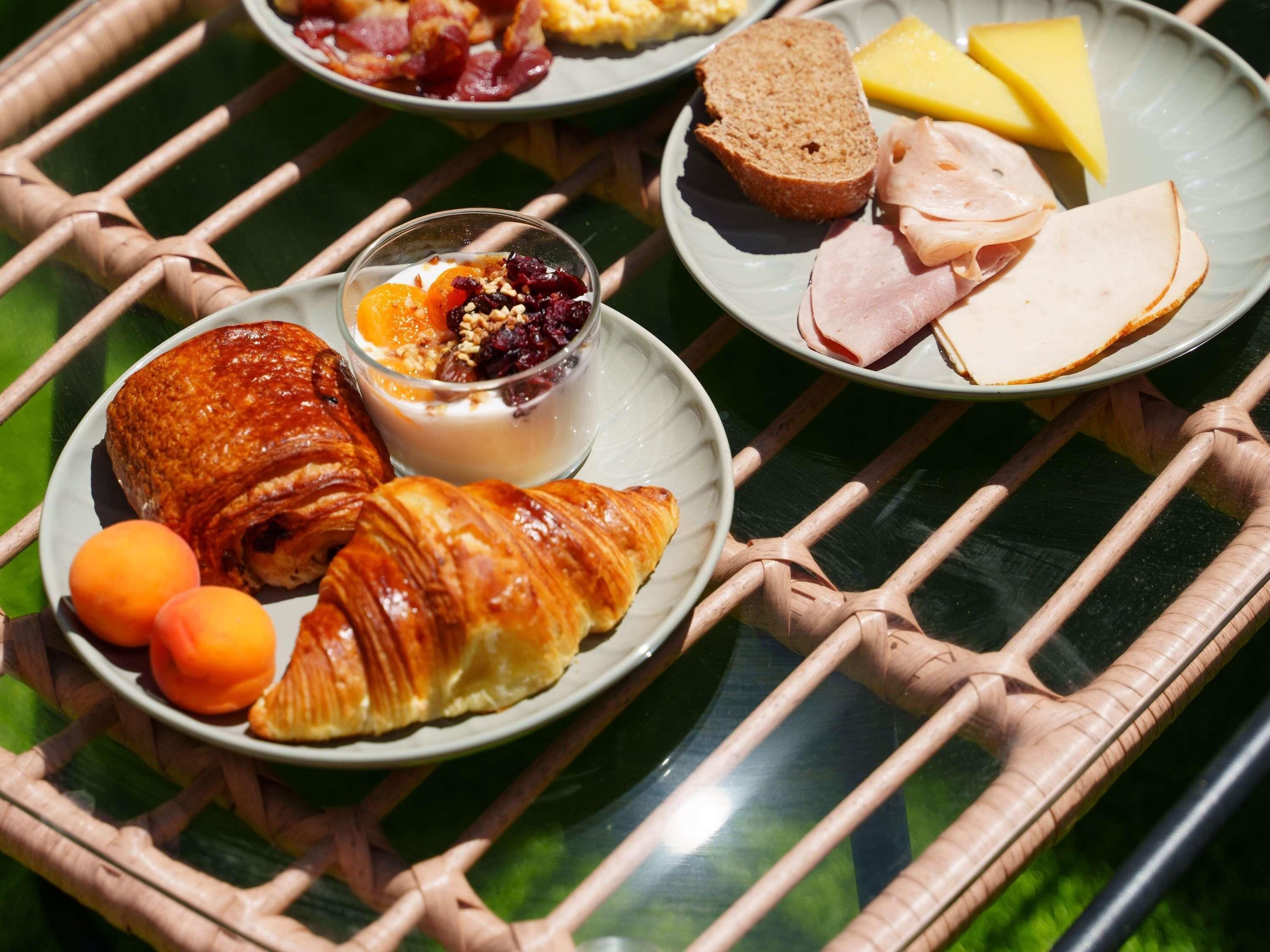 A table with plates of food including croissants, ham, cheese, and fruit.