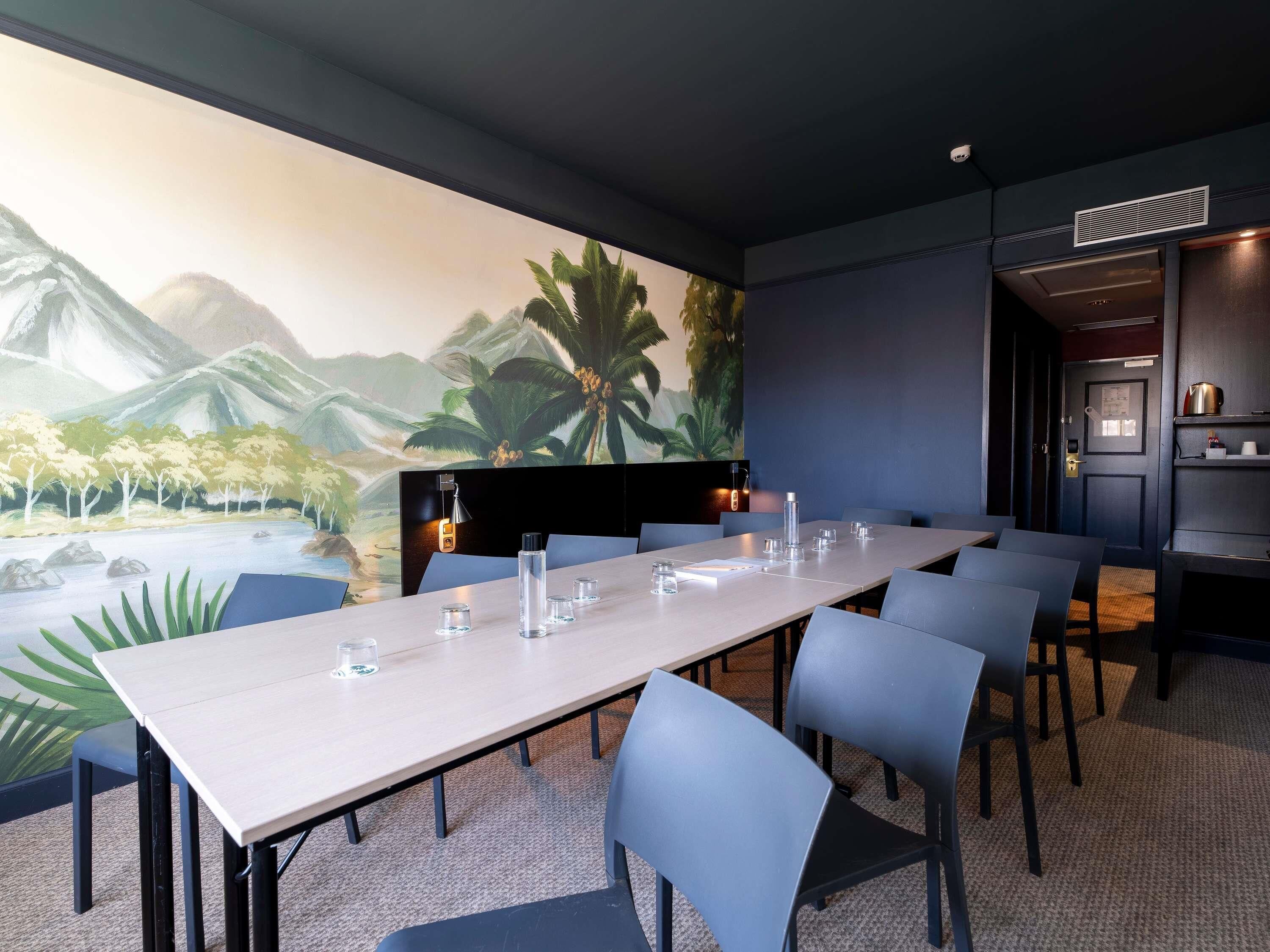 A conference room with a long table, chairs, and a mural of a tropical landscape.