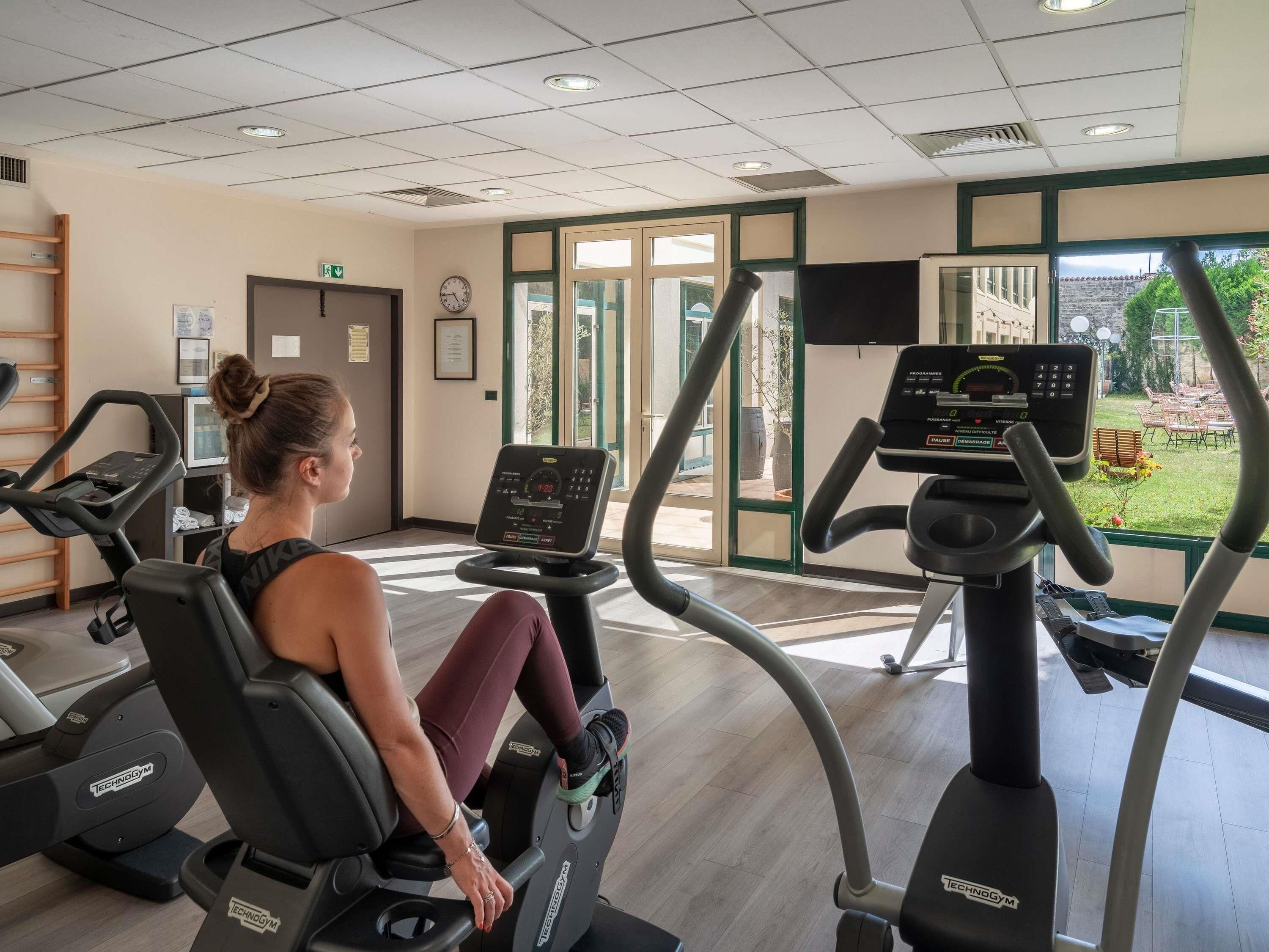 A gym with cardio machines, a clock, and a view of the outdoors.