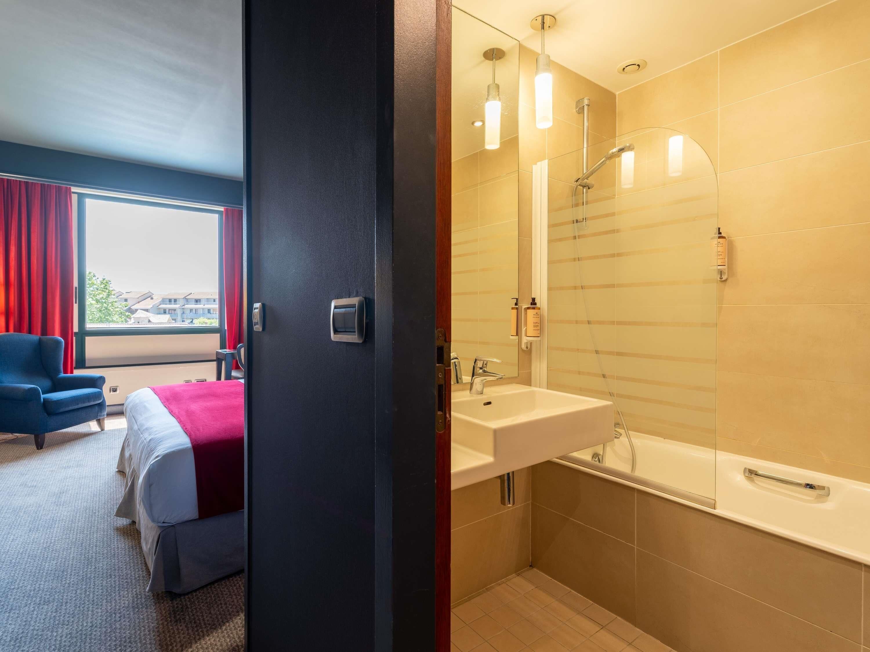 A hotel room with a bed, a desk, and a window with curtains.