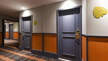 Pasillo de hotel con puertas, piso alfombrado y un letrero amarillo en la pared.