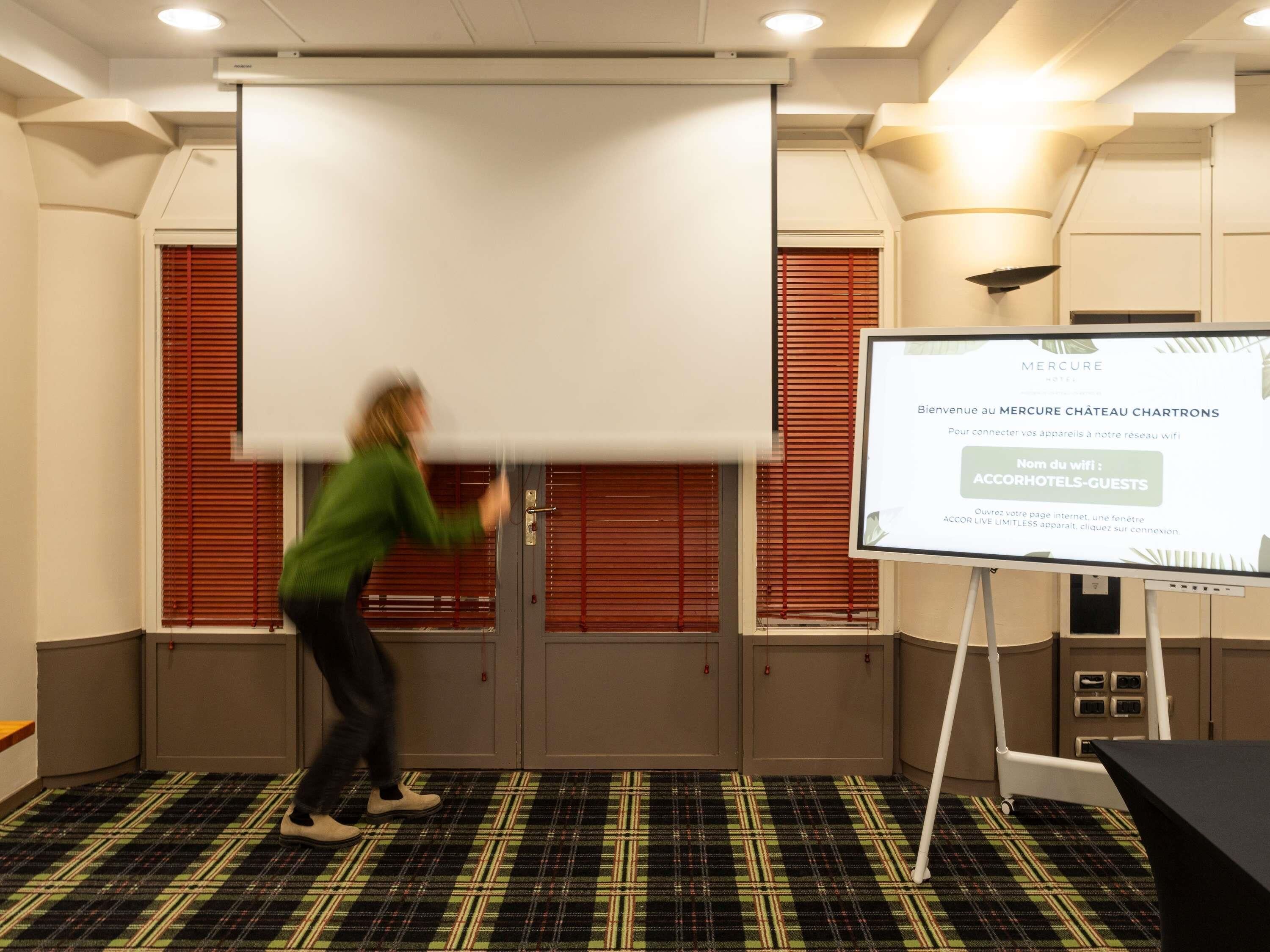 A presentation room with a large white screen, a projection screen, and a whiteboard.