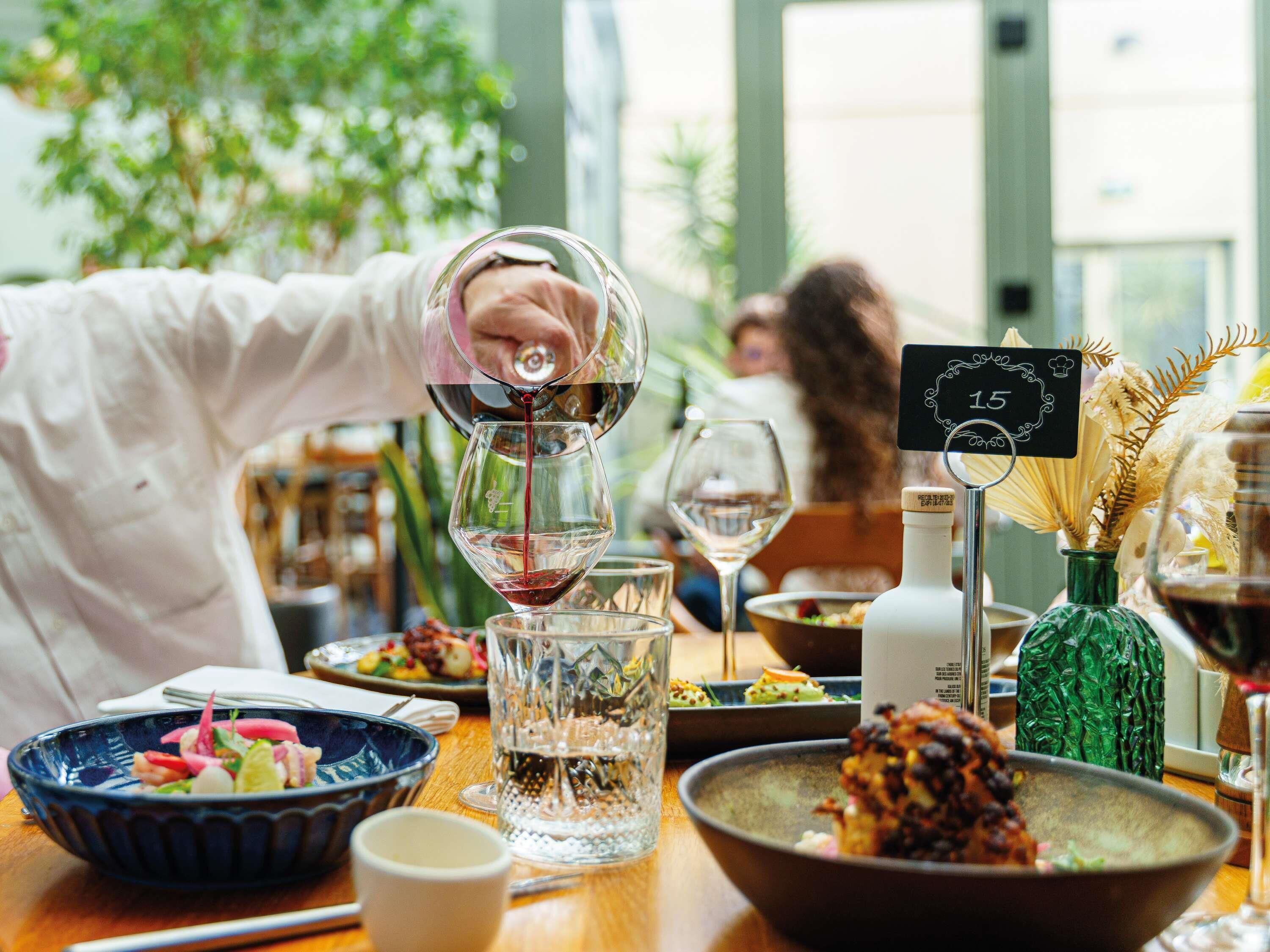 Une table à manger avec différents plats, un verre à vin en cours de remplissage et un panneau indiquant le menu.