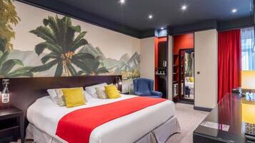 A hotel room with a large bed, a nightstand, a desk, a chair, a bookshelf, and a large mural on the wall.