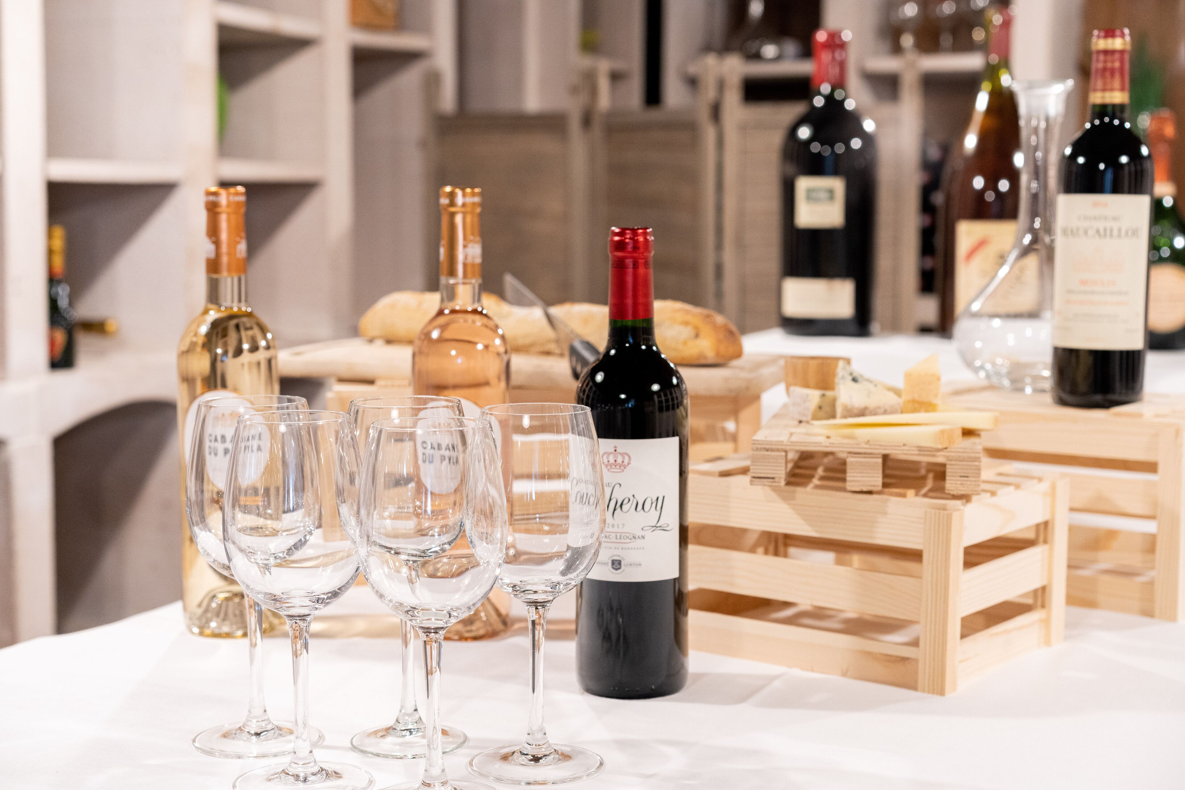Une table avec des verres à vin et des bouteilles, une caisse en bois et du pain.