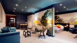 Una habitación de hotel moderna con sofá, sillones, una mesa de comedor, una cama y un mural grande en la pared.