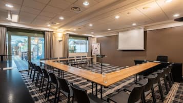 Ein Konferenzraum mit langem Tisch, Stühlen, einer Projektionsleinwand und einem großen Fenster.