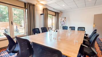 Un salón de conferencias con una larga mesa, sillas negras y ventanas grandes con cortinas.