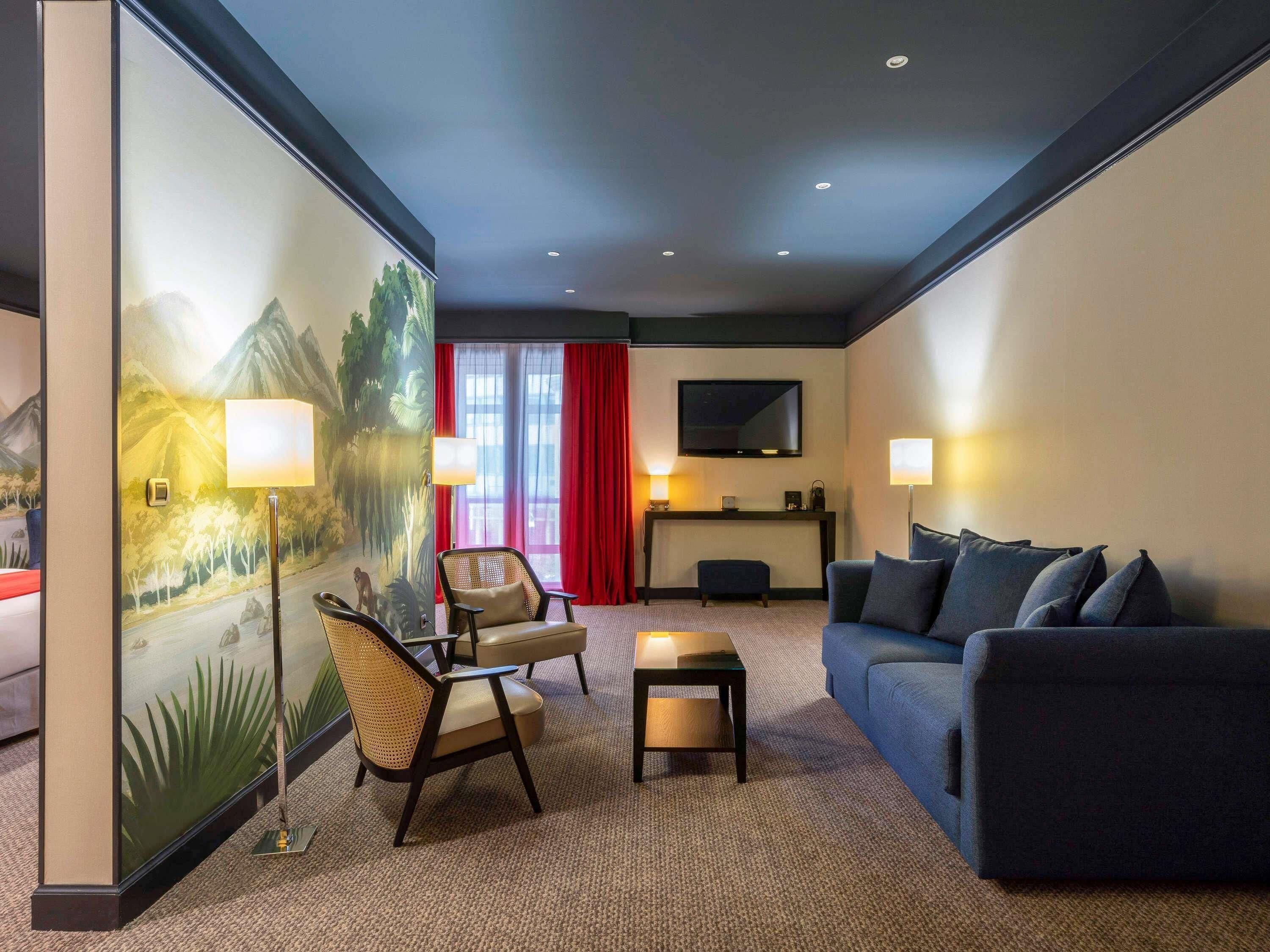 Habitación de hotel con sofá, dos sillones, una mesita, televisión y un cuadro en la pared.