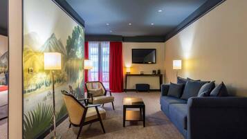 Habitación de hotel con sofá, dos sillones, una mesita, televisión y un cuadro en la pared.