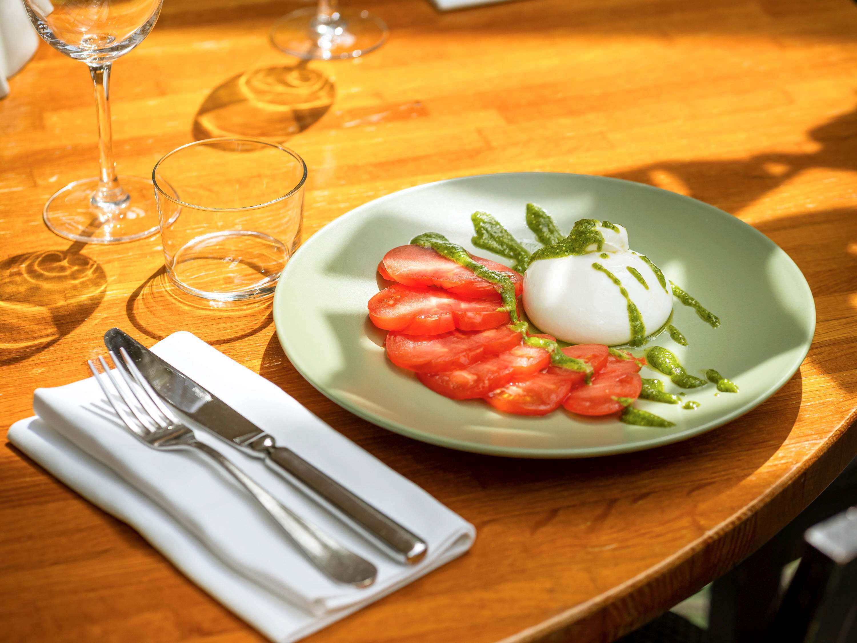Ein Caprese-Salat mit Tomaten, Mozzarella und Basilikum auf einem grünen Teller.