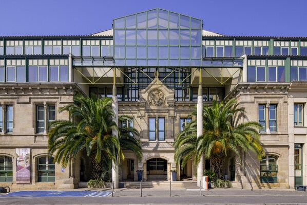 Un edificio histórico con un atrio central de vidrio, palmeras y una fachada de estilo clásico.