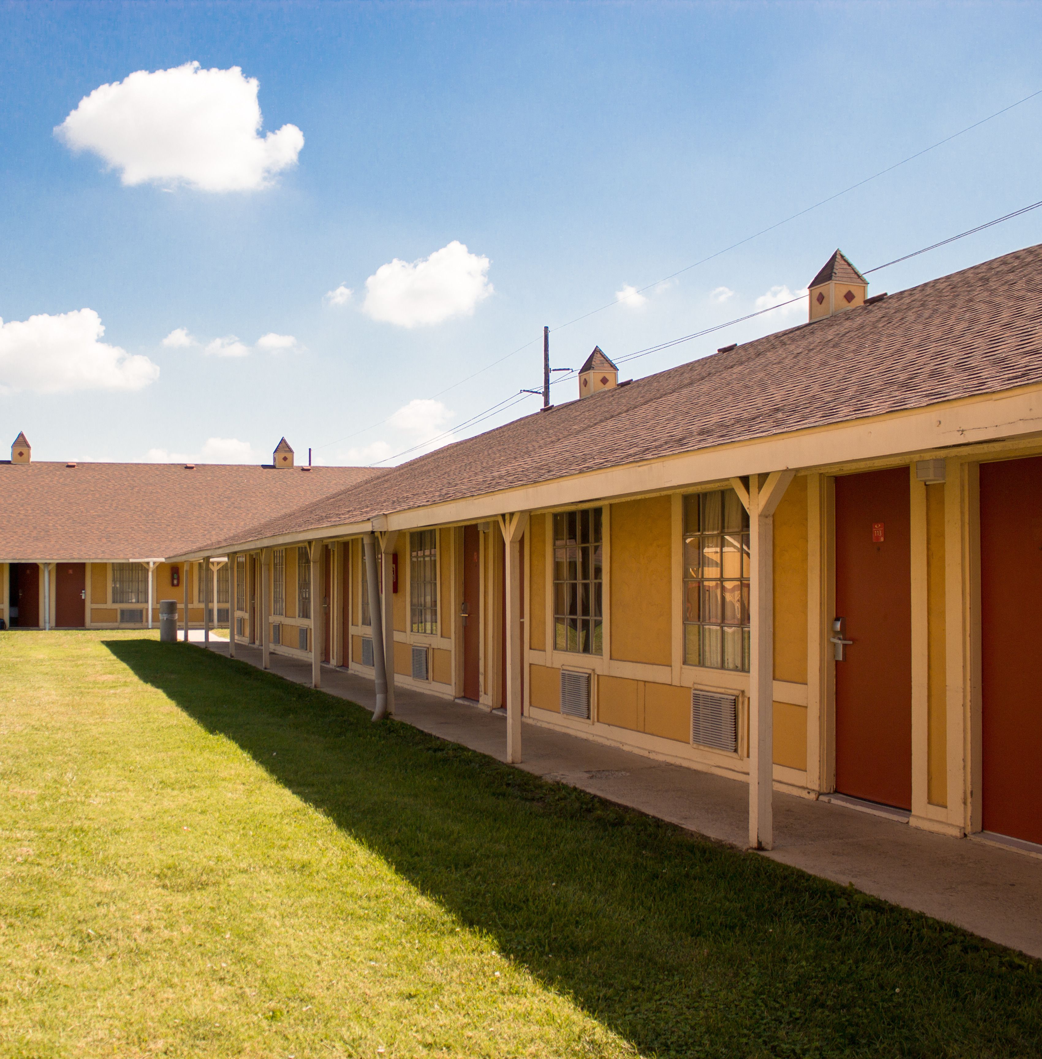 Fila de habitaciones de motel con una galería techada y un área verde al frente.