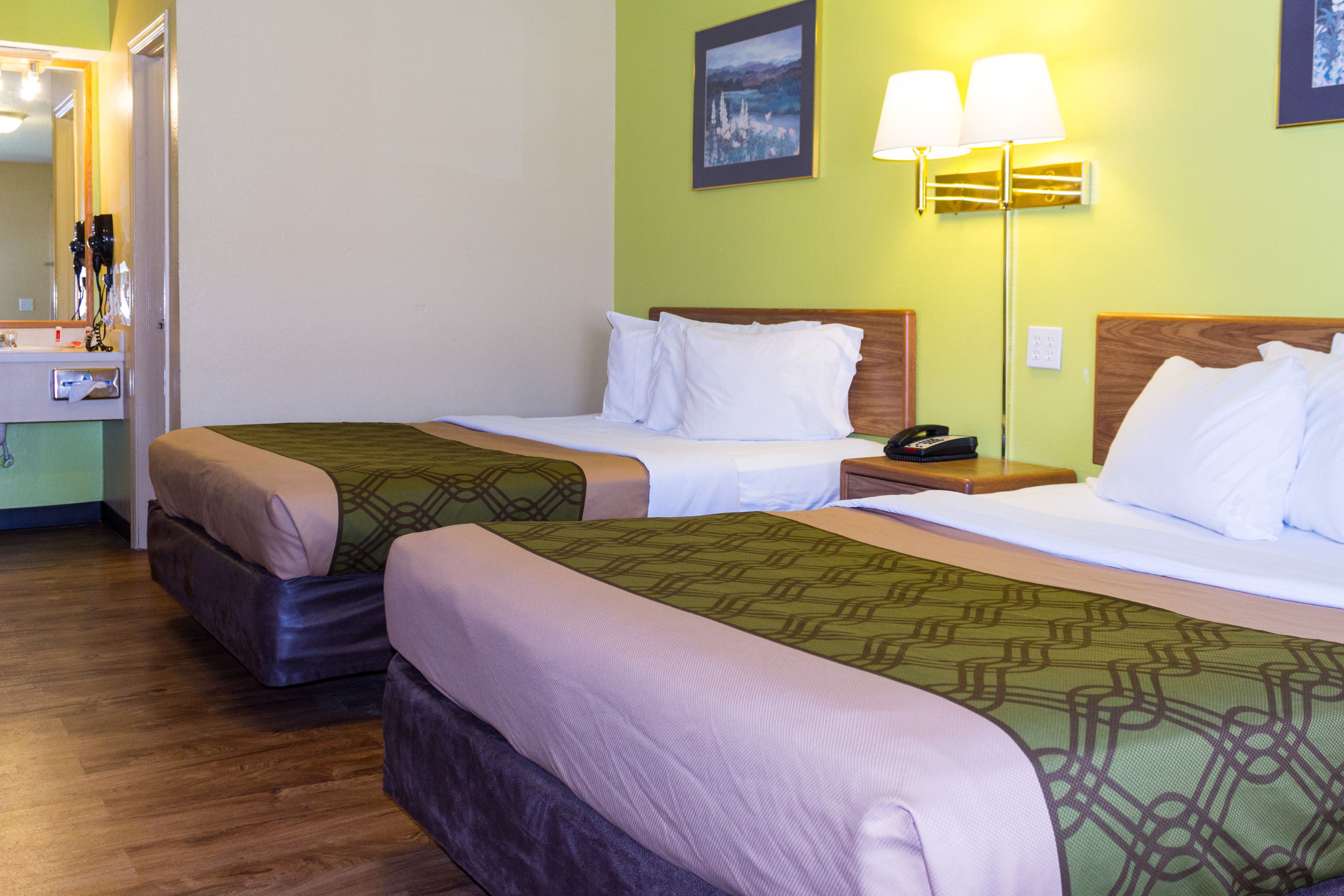 A hotel room with two beds, a bedside table with a lamp, a mirror, and a painting on the wall.