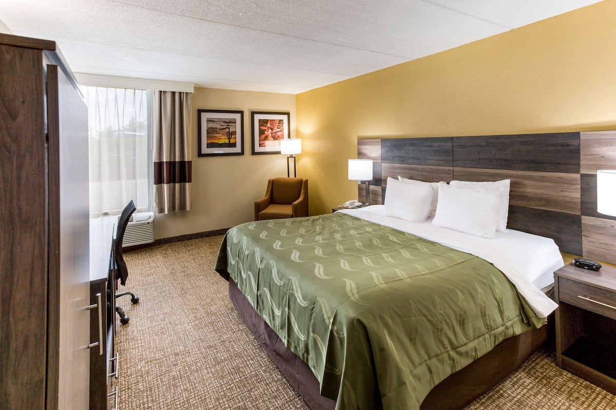 A hotel room with a bed, a desk, a chair, a lamp, and two framed pictures on the wall.
