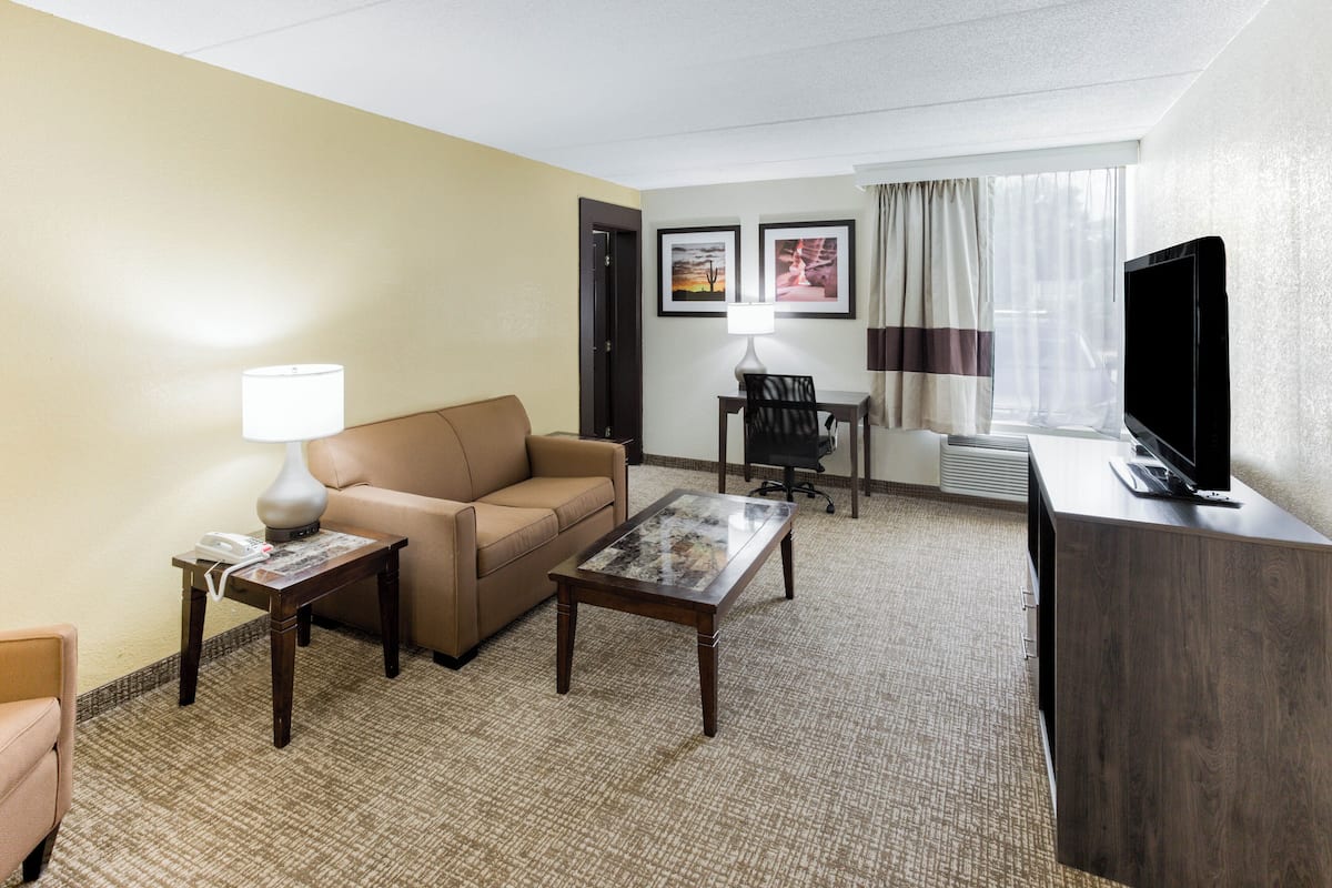 A hotel room with a sofa, a coffee table, a TV, a desk with a lamp, and framed pictures on the wall.