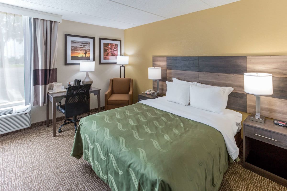 A hotel room with a large bed, two bedside lamps, a desk with a chair, and a window with curtains.