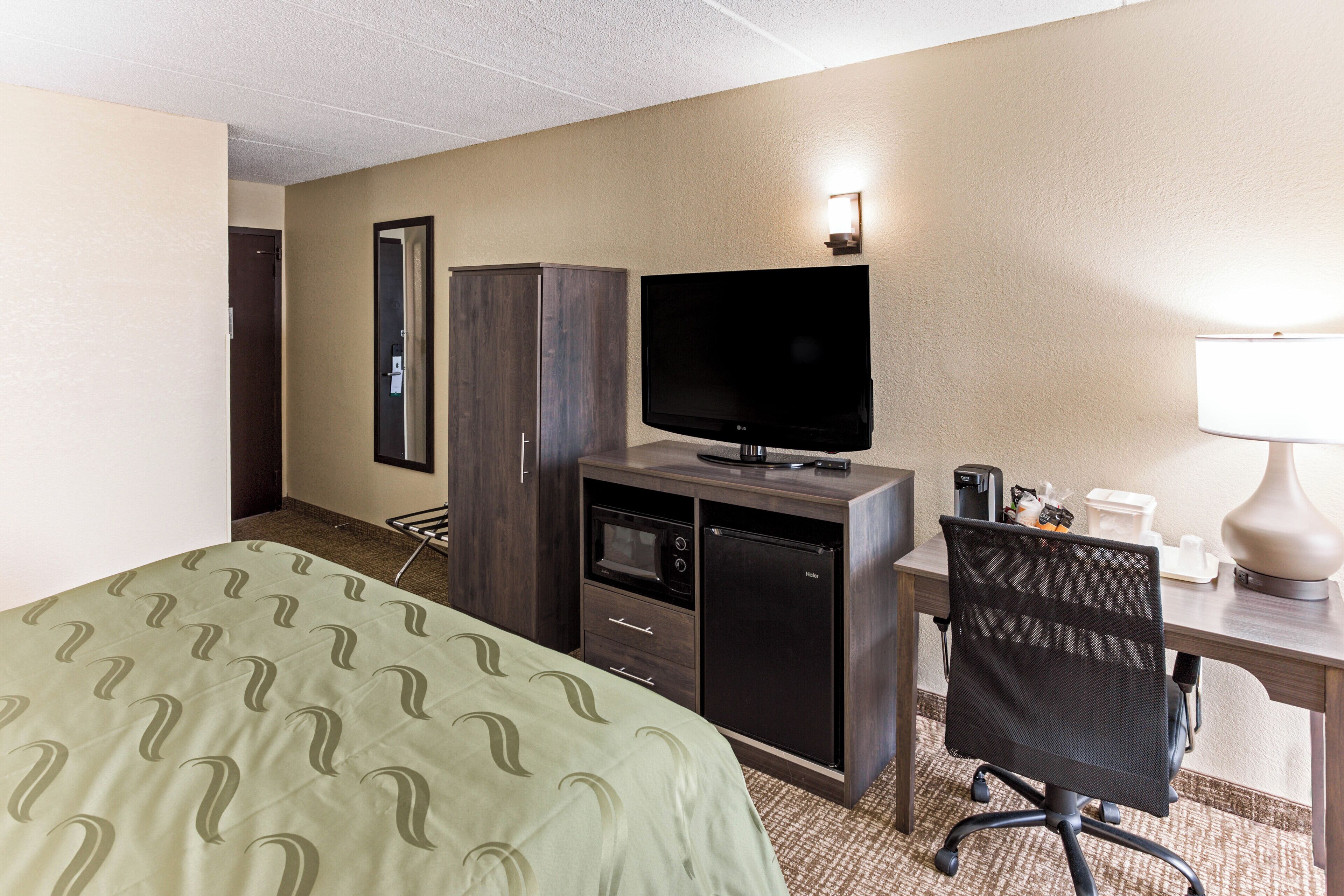Habitación de hotel con cama, escritorio con computadora, televisor, refrigerador y microondas.