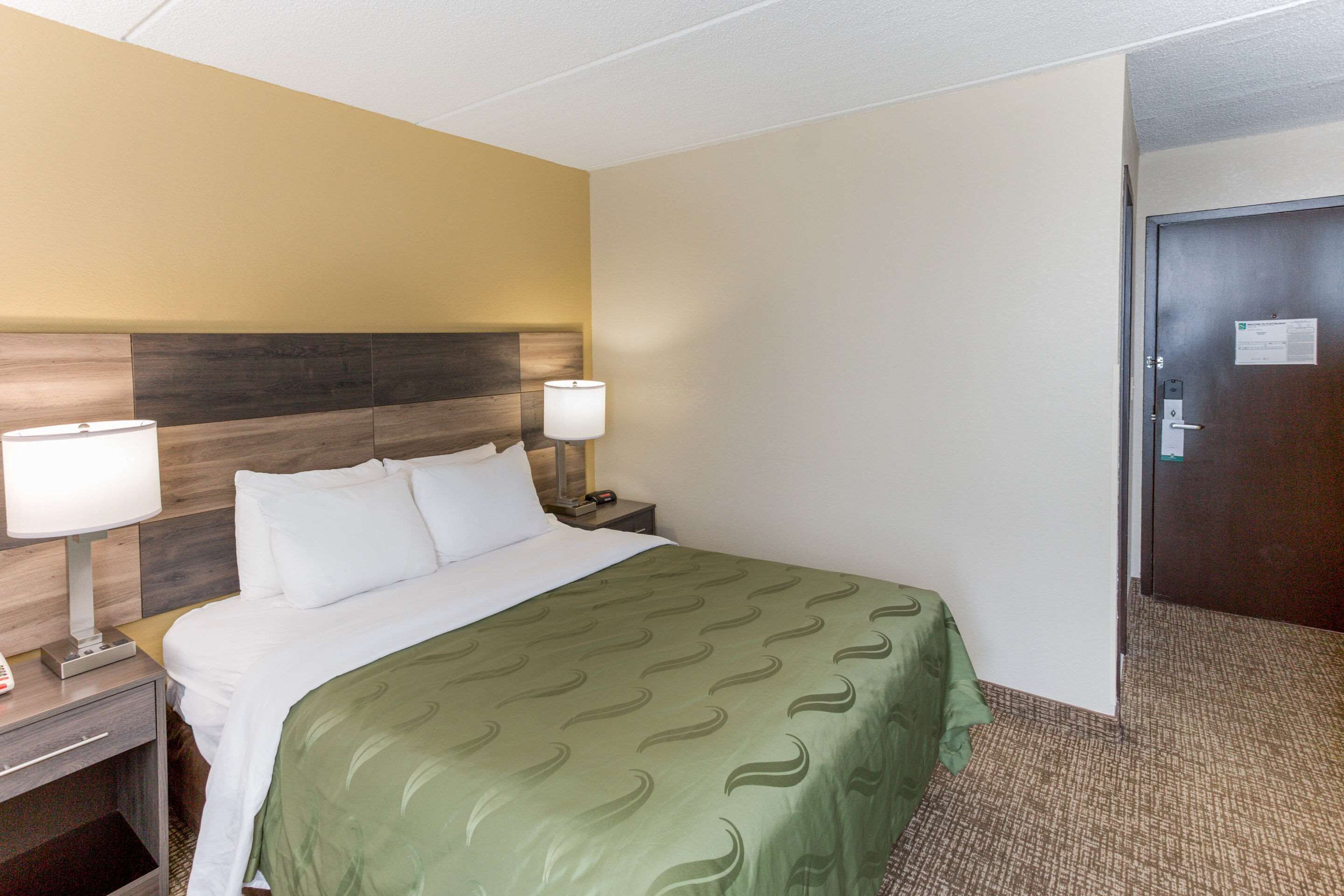Una habitación de hotel con cama, dos lámparas de noche, una mesita de noche y una puerta.