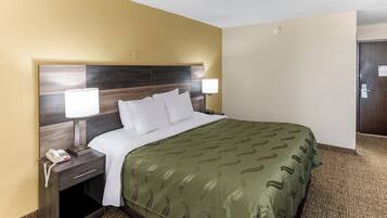 Quarto de hotel com uma cama grande, duas luminárias de cabeceira, mesa de apoio com telefone e piso coberto de carpete.