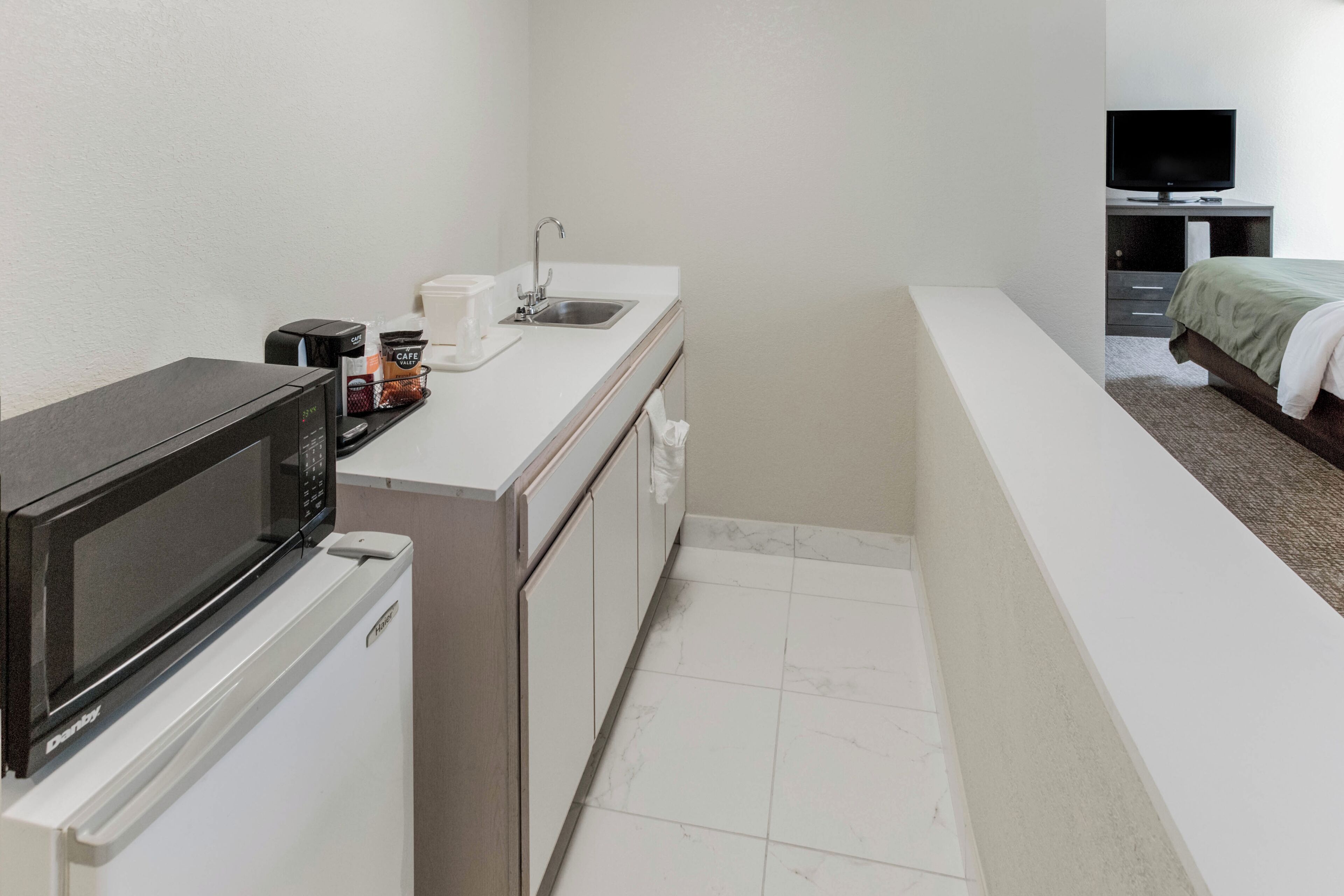 Una kitchenette compacta equipada con microondas, cafetera y lavamanos.