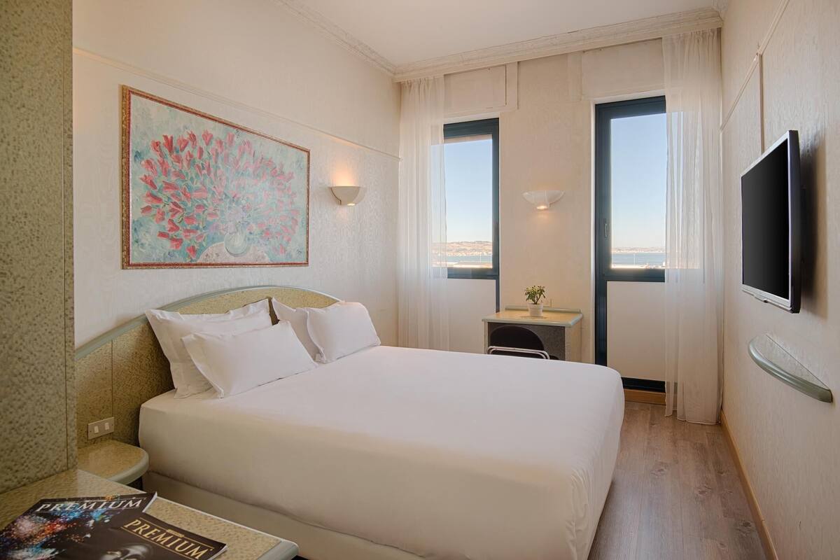 A hotel room with a bed, a desk, a TV, and a painting on the wall.
