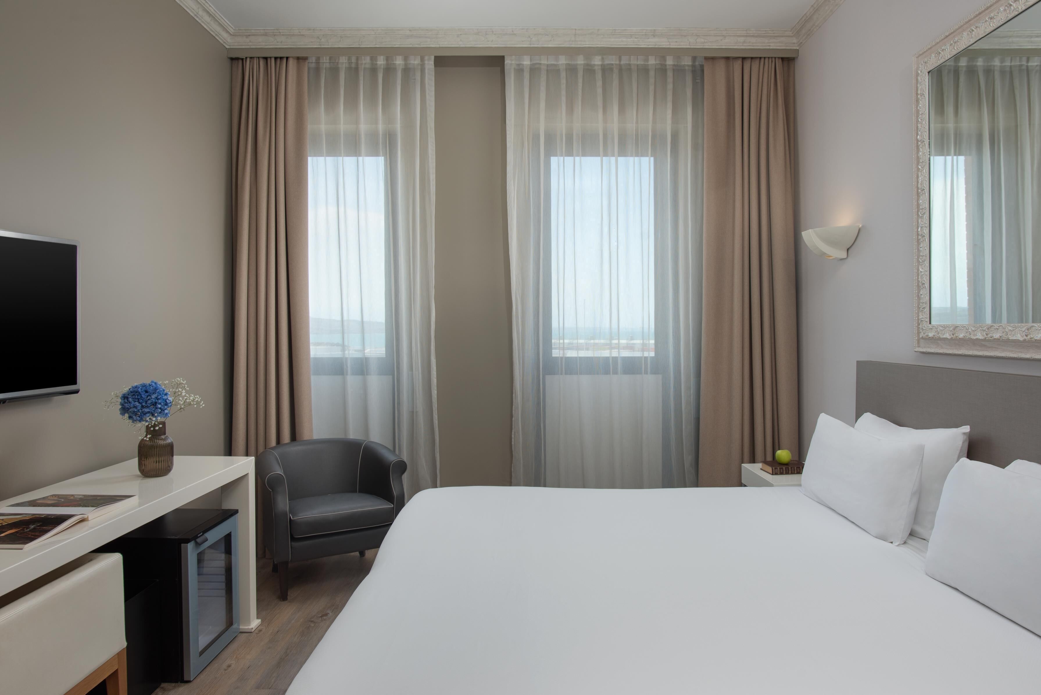 Ein Hotelzimmer mit Bett, Schreibtisch, Stuhl, Fernseher und einem Fenster mit Vorhängen.