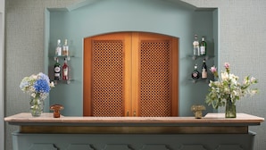 A reception area with a wooden door, a counter, and shelves with bottles and flowers. - NH Ancona (Ancona)