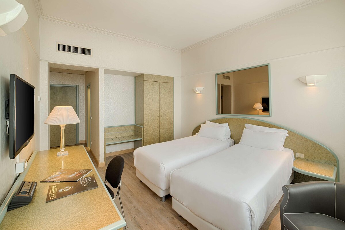 A hotel room with two beds, a desk with a lamp, a television, and a mirror.