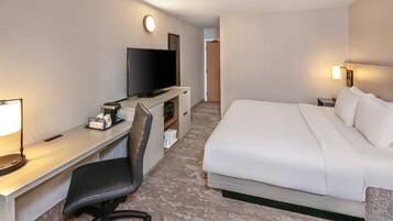 A hotel room with a bed, a desk with a chair, a television, and a nightstand with a lamp.
