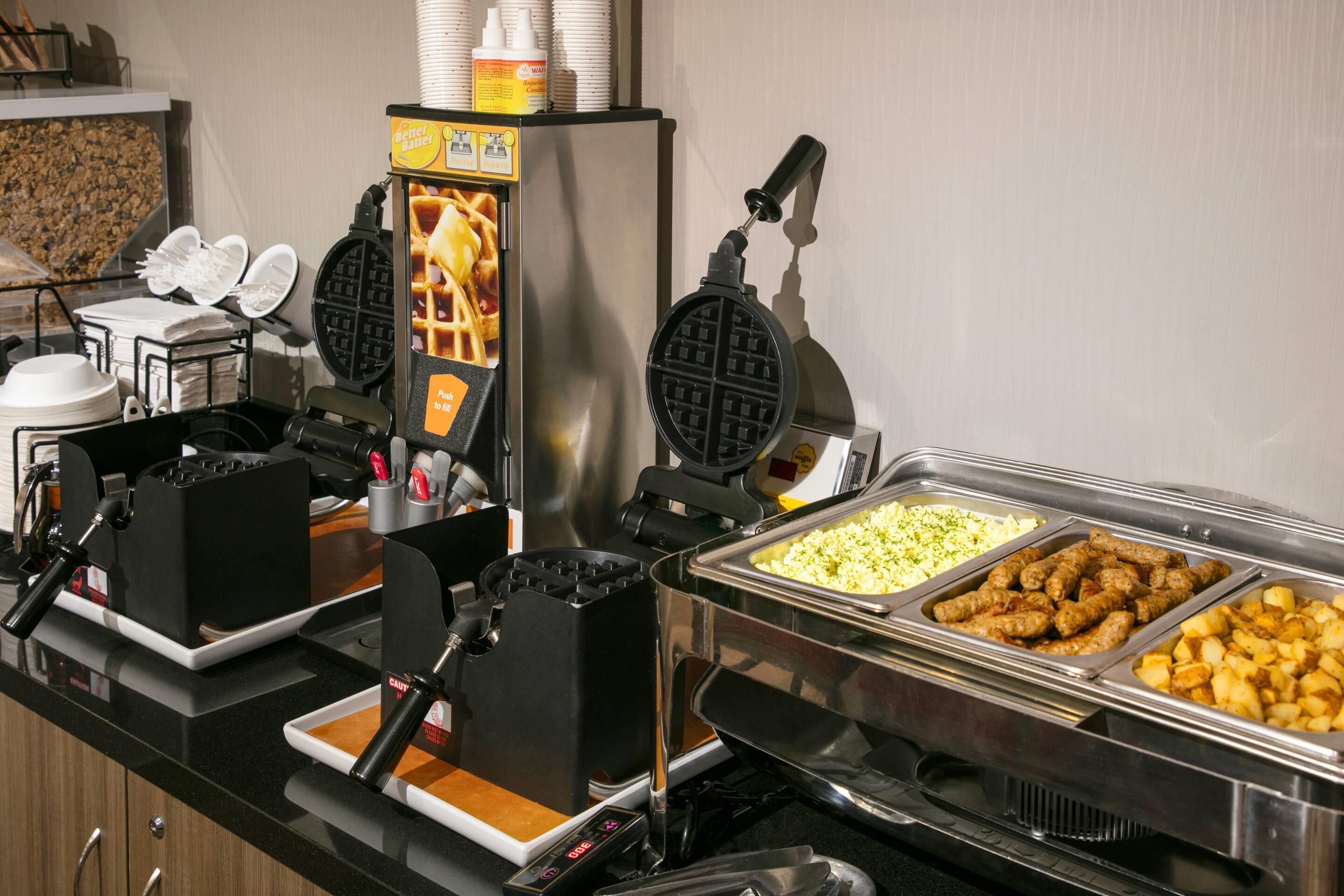 A buffet setup with waffle makers, a coffee machine, and various food items.