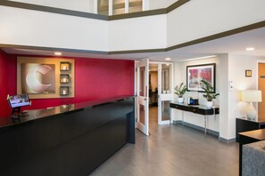 A hotel reception area with a modern design, including a reception desk, a digital screen, and a red accent wall.