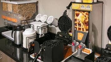 Un angolo dedicato ai waffle, con una piastra per waffle, piatti e una macchina per caffè.